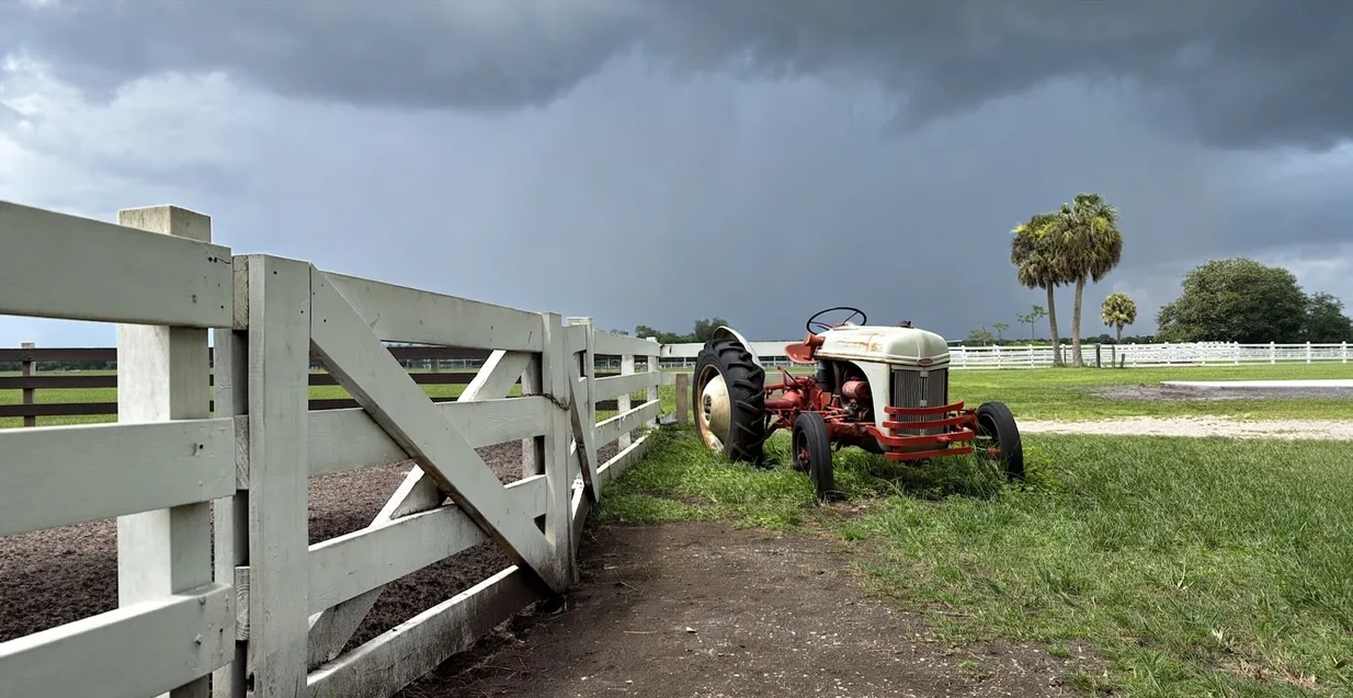 A vintage red and white tractor beside a white fence under storm clouds