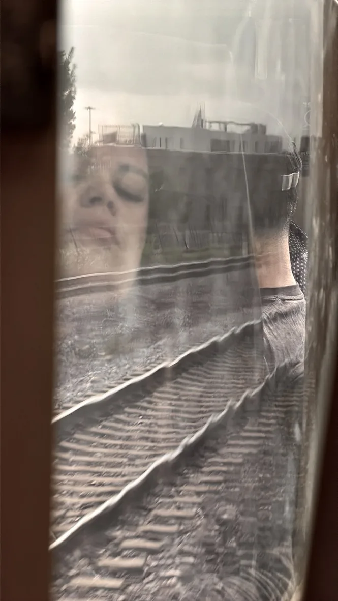 Reflection of a woman's face in a train window above the tracks outside